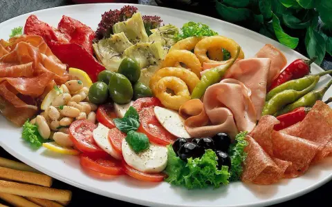 Eine üppige antipasti platte mit Schinken, Salami, Oliven, Artischocken, Tomaten-Mozzarella-Salat und frittierten Ringen.