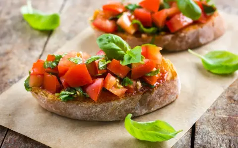 Zwei Bruschetta mit frischen Tomaten und Basilikum, garniert mit einem Hauch von Paprika, auf rustikalem Holz.