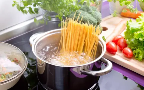 Spaghetti kochen in sprudelndem Wasser. Die richtige **Tagliatelle Kochzeit** ist entscheidend für ein perfektes Pastagericht. Frisches Gemüse wie Brokkoli, Karotten und Tomaten liegen bereit.