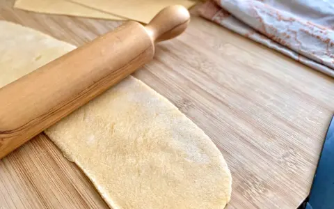 Mit einem Nudelholz wird Teig für **ravioli selber machen ohne maschine** auf einem Holzbrett ausgerollt.
