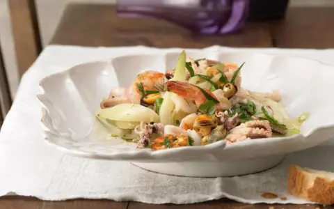 Frischer insalata di mare mit Garnelen, Muscheln und Tintenfischringen, garniert mit Kräutern und Zwiebelringen.