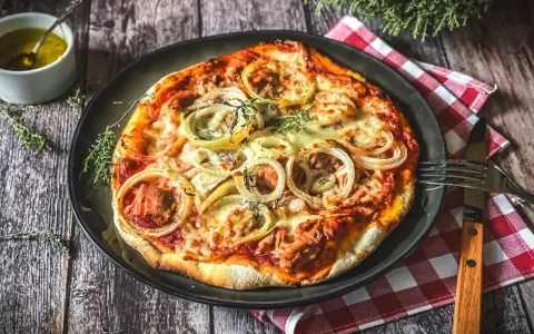 Italienisches Thunfisch Pizza Rezept: Eine köstliche Pizza mit Thunfisch, Zwiebeln und Käse, serviert auf einem Holztisch.