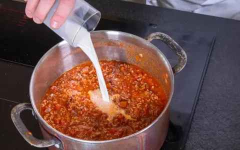 Milch wird in einen Topf mit köchelnder Bolognese gegossen, um die Sauce cremiger zu machen.
