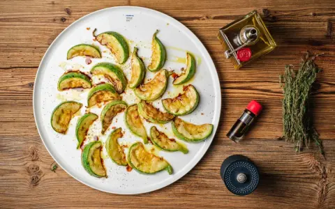 Gebratene Zucchinischeiben auf einem Teller, beträufelt mit Öl und Balsamico. Ein köstlicher Zucchini-Salat, bereit zum Genießen.