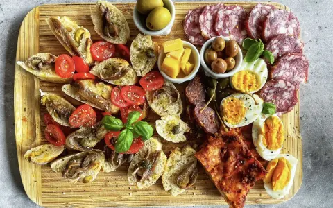 Kaltes italienisches Fingerfood: Bruschetta mit Sardellen, Tomaten, Oliven, Käse, Eiern und Salami auf Holzbrett.