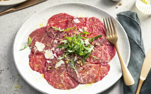 Carpaccio selber machen: hauchdünne Rinderfiletscheiben mit Rucola, Parmesan und Pinienkernen auf einem Teller.