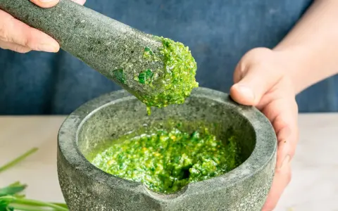 Frische Kräuter werden im Mörser zermahlen, um zu zeigen, wie man Pesto zubereitet.