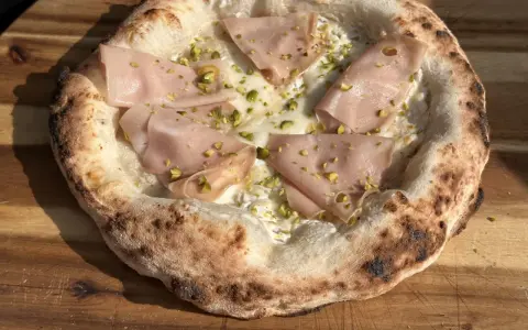 Pizza mit Mortadella und Pistazien auf luftigem pizzateig mit hefe. Der Rand ist knusprig und leicht verbrannt.