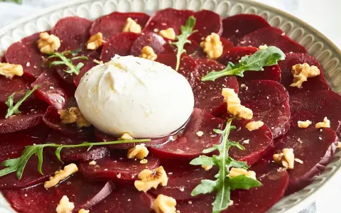 Rote Bete Carpaccio mit Burrata, Walnüssen und Rucola. Ein köstlicher Salat, der auf einem Teller serviert wird.
