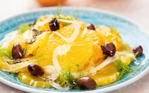 Erfrischender orangensalat sizilianisch mit Fenchel und dunklen Oliven auf einem blauen Teller.