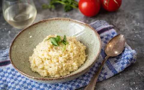 Cremiges Risotto, perfekt als Grundrezept für viele Variationen. Mit frischer Petersilie garniert, daneben ein Glas Weißwein und Tomaten.