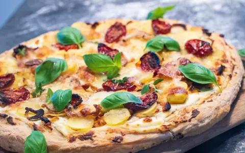 Leckeres Pizza Bianca Rezept mit Kartoffelscheiben, getrockneten Tomaten und frischem Basilikum.
