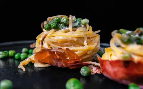 Köstliche italienische Pasta Vorspeisen mit Erbsen und Schinken, auf einem dunklen Teller angerichtet.