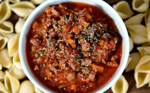 Herzhafte pancetta bolognese in einer Schüssel, umgeben von ungekochten Muschelnudeln.