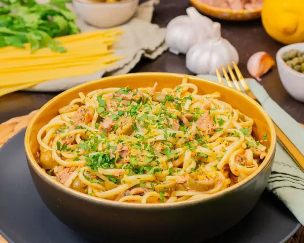 Eine Schüssel mit Thunfisch Pasta, garniert mit Petersilie und Zitronenschale. Oliven und Kapern sind ebenfalls sichtbar.