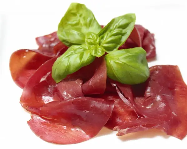 Dünne Scheiben von Bresaola, einem luftgetrockneten Rindfleisch, garniert mit frischem Basilikum.