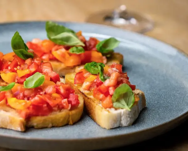 Drei Scheiben geröstetes Brot, belegt mit frischen Tomaten und Basilikum. Ein authentisches rezept bruschetta original italienisch.