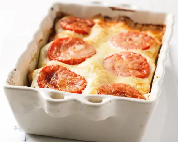 Gorgonzola Lasagne mit Tomaten und geschmolzenem Käse in einer weißen Auflaufform.