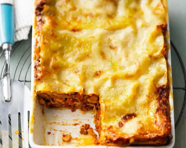 Eine goldbraun überbackene Lasagne mit einer cremigen Käseschicht. Ein Stück ist bereits entnommen, was die saftige Füllung offenbart. Diese Pistazien Lasagne sieht köstlich aus!