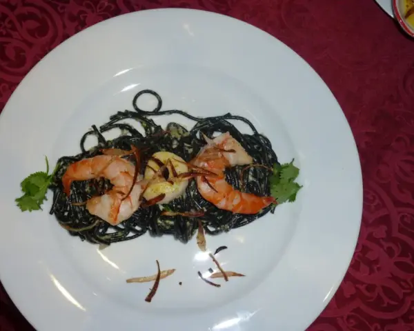 Schwarze Spaghetti mit Garnelen, garniert mit Koriander und knusprigen Zwiebeln. Ein köstliches Gericht, das auf einem weißen Teller serviert wird.