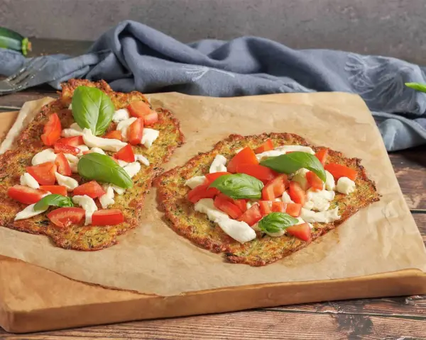Zwei leckere Zucchini-Pizzen mit Mozzarella, Tomaten und Basilikum auf Backpapier.