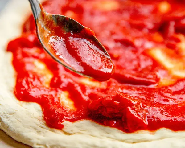 Eine Löffelspitze verteilt die original italienische pizzasauce auf einem Pizzateig.