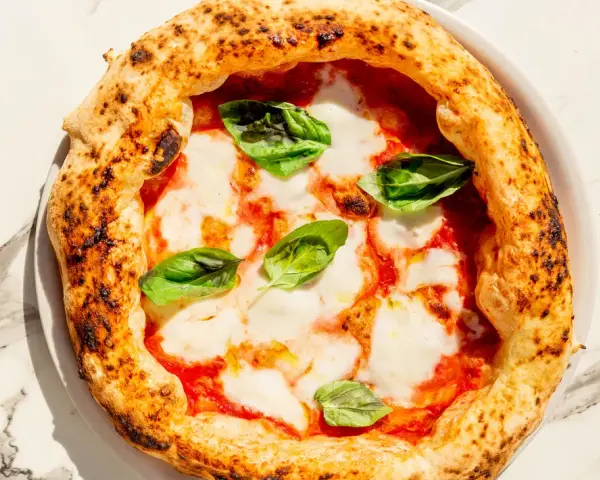 Eine echte italienische Pizza Margherita mit geschmolzenem Mozzarella, Tomatensauce und frischem Basilikum auf einem Marmortisch.