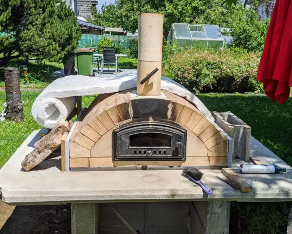 Ein selbstgebauter Pizzaofen im Garten, noch in der Bauphase, mit Isolierung und Schornstein. Bald bereit für die erste Pizza!
