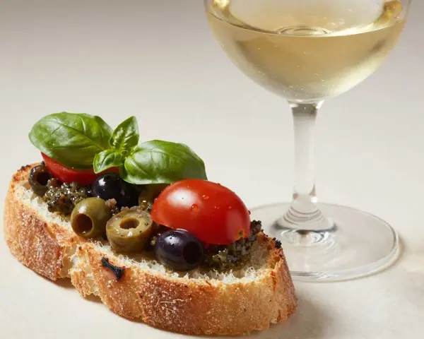 Bruschetta mit Olivencreme, Tomaten und Basilikum. Ein Glas Weißwein daneben. Perfekt für ein schnelles olivencreme rezept.
