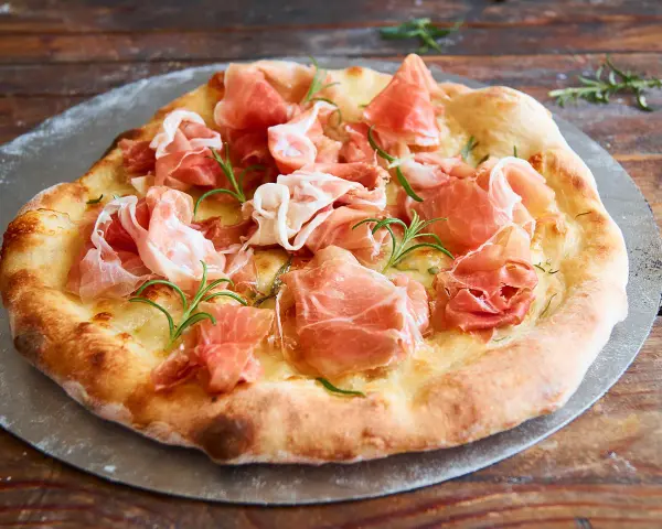 Eine köstliche biancaneve pizza mit zartem Schinken und Rosmarin, auf einem Pizzastein serviert.