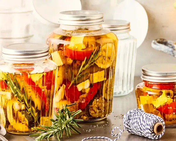 Drei Gläser mit italienischem Fingerfood: eingelegtes Gemüse wie Paprika und Zucchini mit Kräutern in Öl.
