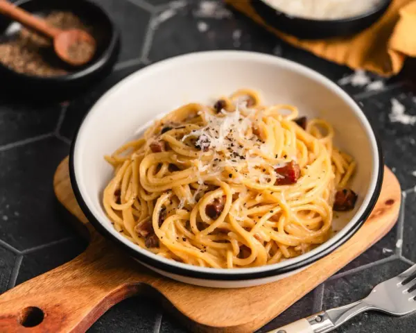Eine Schüssel cremiger Pasta Carbonara, garniert mit frisch geriebenem Parmesan und schwarzem Pfeffer, bereit zum Genießen.