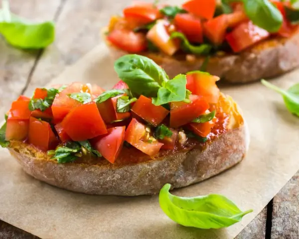 Zwei Bruschetta mit frischen Tomaten und Basilikum, garniert mit einem Hauch von Paprika, auf rustikalem Holz.