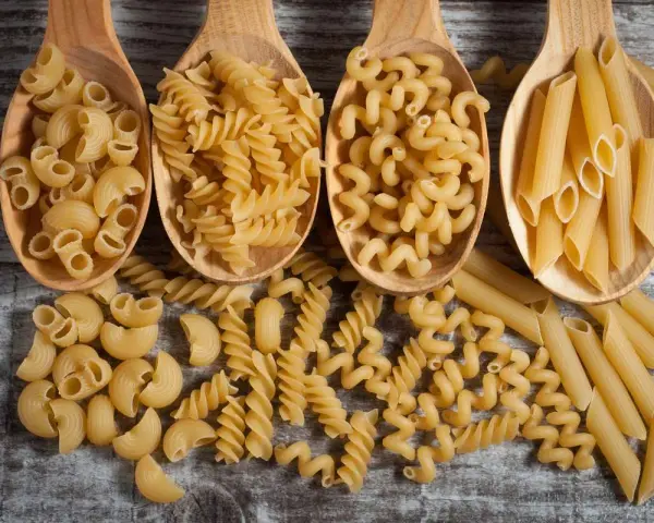 Vier Holzlöffel mit verschiedenen Nudelsorten: Maccheroni, Fusilli, Cavatappi und Penne. Die perfekte Menge Nudeln pro Person für ein köstliches Essen.