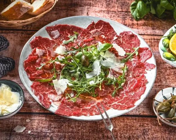 Carpaccio: hauchdünne Rindfleischscheiben mit Rucola, Parmesan und Kapern. Ein Klassiker der italienischen Küche.
