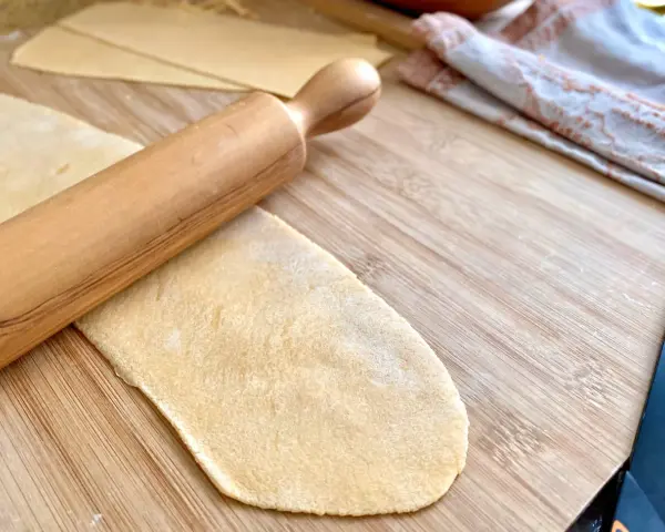 Mit einem Nudelholz wird Teig für **ravioli selber machen ohne maschine** auf einem Holzbrett ausgerollt.