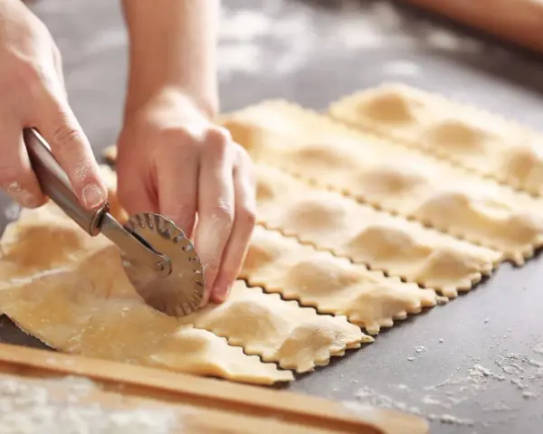 Hände schneiden mit einem Teigrädchen frische Ravioli. Das sind die besten Ravioli Rezepte zum Nachmachen.