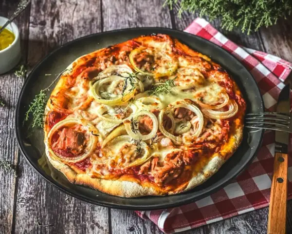 Italienisches Thunfisch Pizza Rezept: Eine köstliche Pizza mit Thunfisch, Zwiebeln und Käse, serviert auf einem Holztisch.