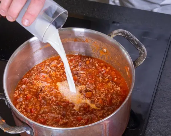 Milch wird in einen Topf mit köchelnder Bolognese gegossen, um die Sauce cremiger zu machen.