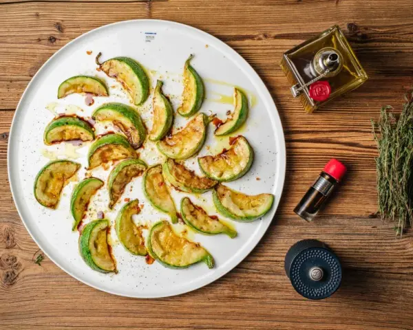 Gebratene Zucchinischeiben auf einem Teller, beträufelt mit Öl und Balsamico. Ein köstlicher Zucchini-Salat, bereit zum Genießen.