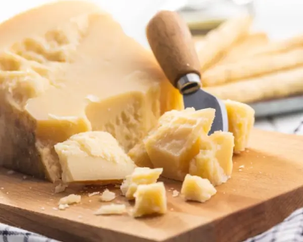 Ein Stück Parmesan mit grob abgebrochenen Stücken und einem Käsemesser. Die Parmesan Rinde ist sichtbar.