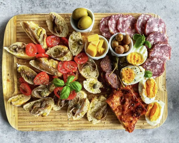 Kaltes italienisches Fingerfood: Bruschetta mit Sardellen, Tomaten, Oliven, Käse, Eiern und Salami auf Holzbrett.