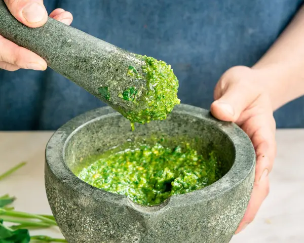Frische Kräuter werden im Mörser zermahlen, um zu zeigen, wie man Pesto zubereitet.