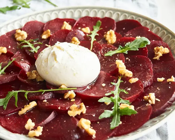 Rote Bete Carpaccio mit Burrata, Walnüssen und Rucola. Ein köstlicher Salat, der auf einem Teller serviert wird.