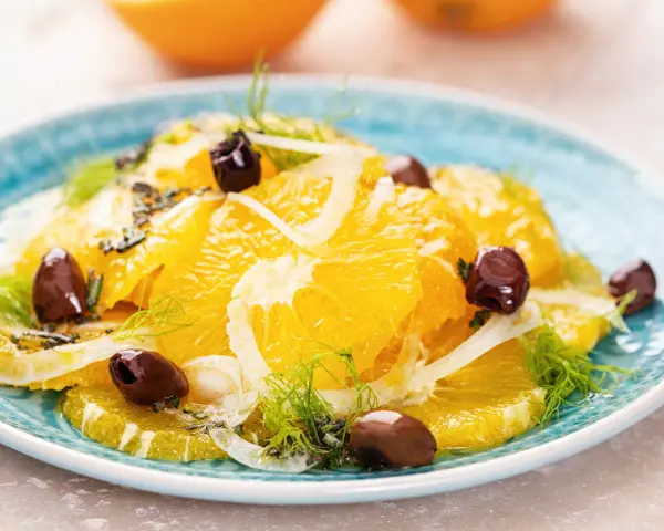 Erfrischender orangensalat sizilianisch mit Fenchel und dunklen Oliven auf einem blauen Teller.