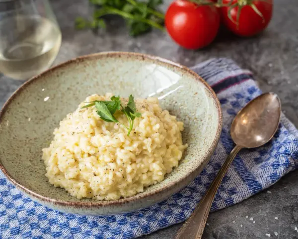 Cremiges Risotto, perfekt als Grundrezept für viele Variationen. Mit frischer Petersilie garniert, daneben ein Glas Weißwein und Tomaten.