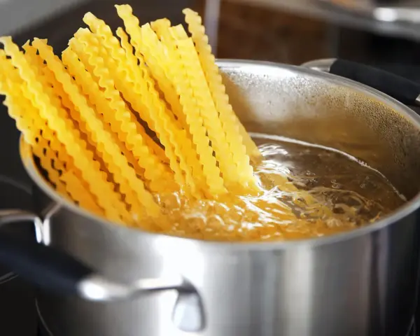 Lange, gewellte vermicelli noodles kochen in sprudelndem Wasser in einem Edelstahltopf.