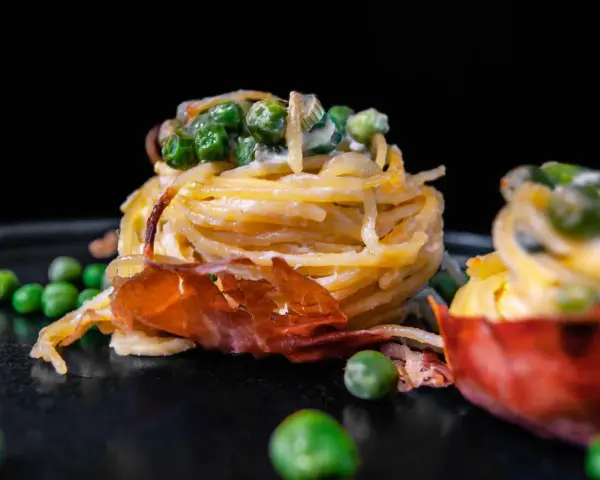 Köstliche italienische Pasta Vorspeisen mit Erbsen und Schinken, auf einem dunklen Teller angerichtet.