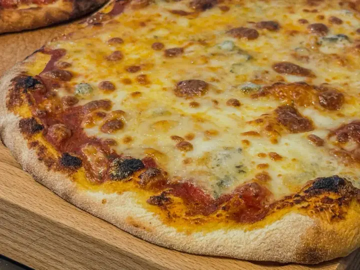 Eine köstliche quattro formaggi Pizza mit geschmolzenem Käse und knusprigem Rand auf einem Holzbrett.