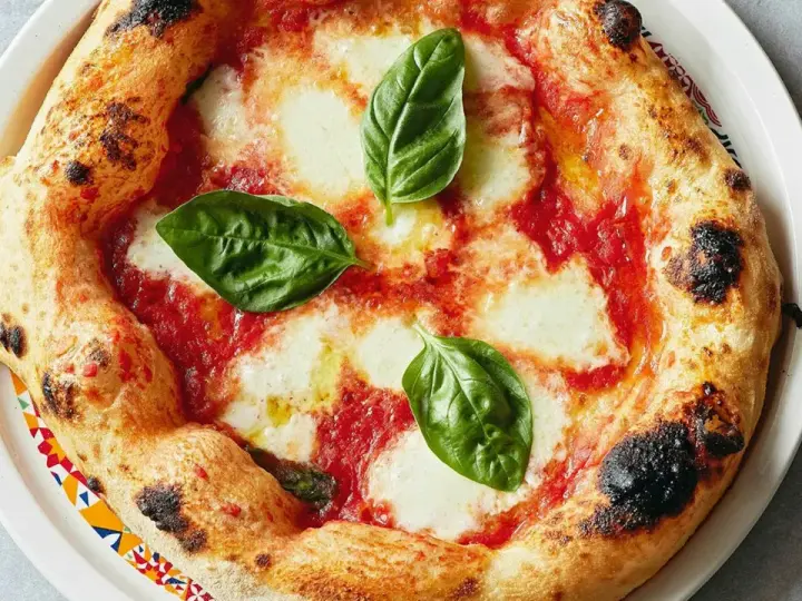 Eine original Pizza Margherita mit geschmolzenem Mozzarella, Tomatensauce und frischem Basilikum. Der Rand ist goldbraun und leicht angekohlt.